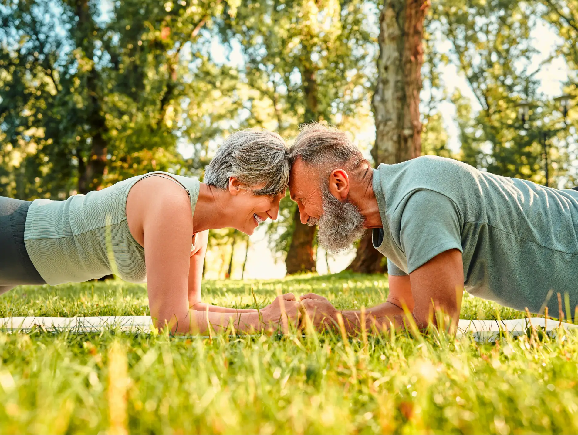 Ein Paar macht gemeinsam eine Unterarmstütz-Übung (Plank) auf einer Matte im sonnigen Gras.